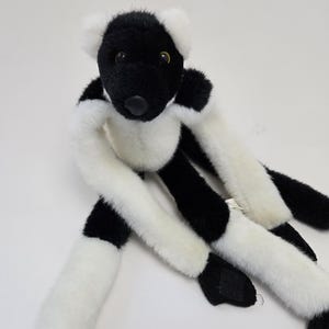 Può includere: Giocattolo di peluche di lemuri nero e bianco con grandi occhi neri e un naso nero. Il lemuri è seduto con le gambe distese.