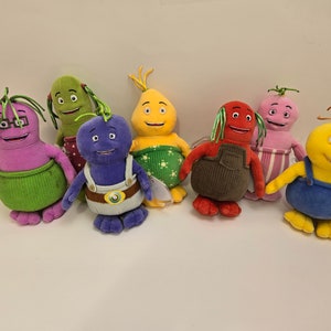 Peut inclure: Un ensemble de sept peluches en forme de différents légumes. Les peluches sont toutes de couleurs différentes et ont des visages amicaux. Elles portent toutes des tenues différentes, y compris une salopette, une jupe et une robe.