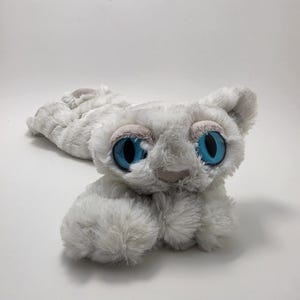 May include: A plush toy shaped like a creature with long, soft, light gray fur. It features large, round, bright blue eyes with dark pupils and light gray eyelids. The creature has a small, rounded nose and pointed ears, with a long, slender body.