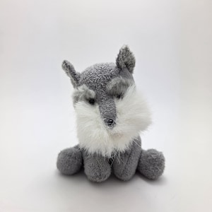 May include: A small gray and white plush toy dog with a fluffy white beard. The dog is sitting with its paws tucked under its body.