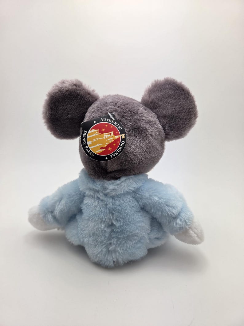 May include: A plush toy mouse with large gray ears and a light blue jacket. The toy has a tag that reads "Disney Parks Authentic Original". The toy is made of soft, fuzzy material.
