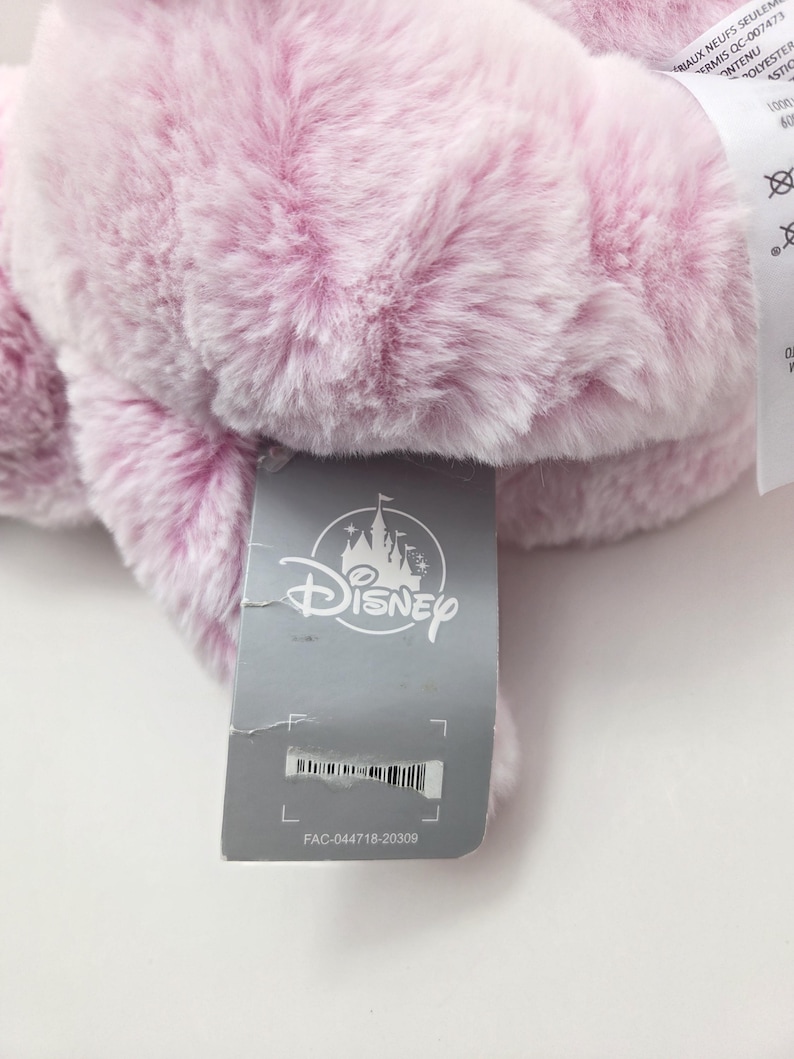 May include: A pink plush Disney character with a gray tag that reads "Disney" and "FAC-044718-20309".