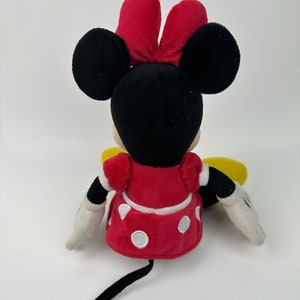 K&ouml;nnte beinhalten: Ein Pl&uuml;schtier von Minnie Mouse, das sitzt. Sie tr&auml;gt ein rotes Kleid mit wei&szlig;en Punkten und eine rote Schleife. Ihre Ohren sind schwarz und ihr Schwanz ist schwarz.