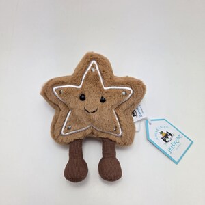 Peut inclure: Un jouet en peluche marron en forme d'étoile avec un visage souriant, des coutures blanches et deux jambes marron. Le jouet porte une étiquette "Jellycat London".