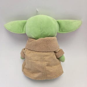 May include: A green plush toy with large ears and a brown coat. The toy is a popular character from the Star Wars franchise.