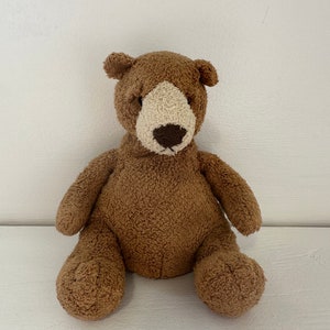 Puede incluir: Un oso de peluche marrón con la cara blanca y la nariz marrón. El oso está sentado sobre una superficie blanca.