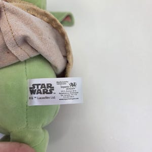 May include: Green plush toy of a Star Wars character with a brown hooded robe. The tag reads "STAR WARS" and "&copy; & &trade; Lucasfilm Ltd."