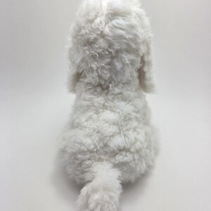 May include: A plush, white stuffed dog toy, viewed from the back. The toy has a fluffy, curly texture, with visible ears and a small, curled tail. The dog is positioned against a plain white background.