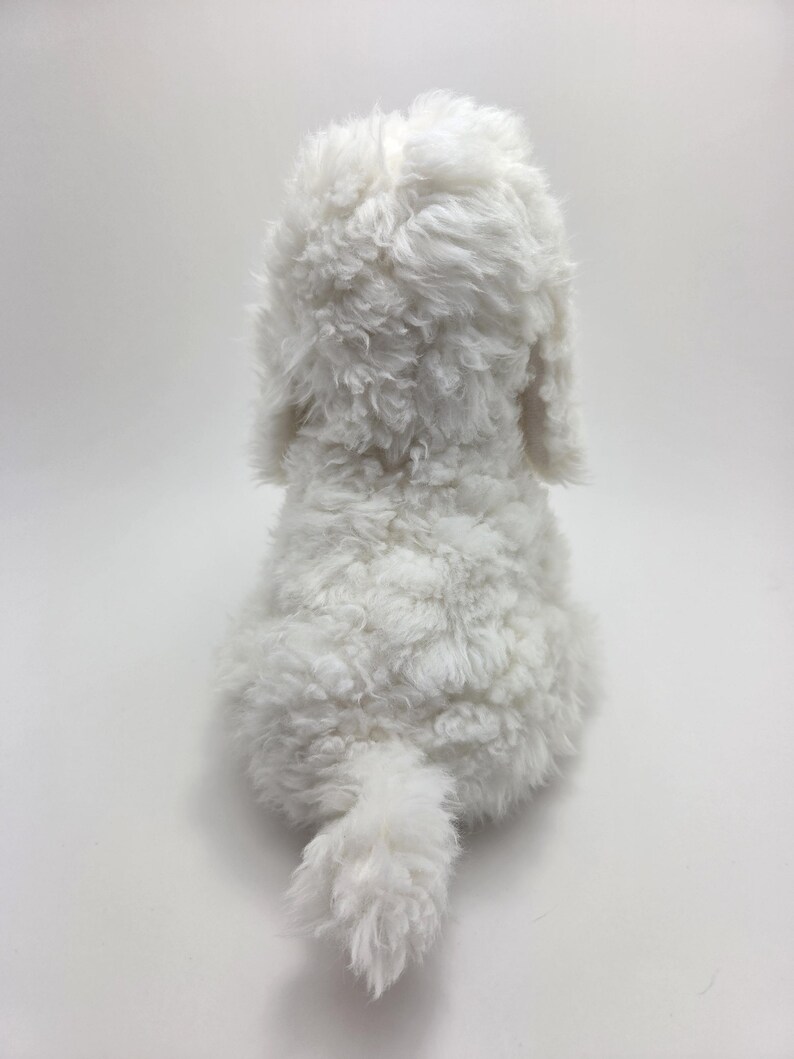 May include: A plush, white stuffed dog toy, viewed from the back. The toy has a fluffy, curly texture, with visible ears and a small, curled tail. The dog is positioned against a plain white background.