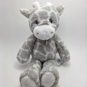 以下が含まれることがあります： グレーと白のぬいぐるみキリン。 ぬいぐるみは、斑点模様、白いマズル、小さな耳が特徴です。 キリンは足を伸ばして座っており、子供向けの抱きしめたくなるおもちゃです。