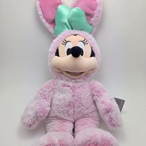 May include: Pink plush bunny rabbit with a green bow, wearing a pink bunny costume with paw prints on the feet.