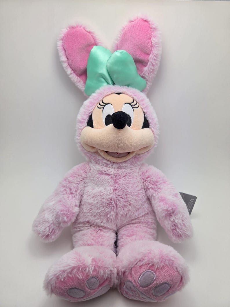 May include: Pink plush bunny rabbit with a green bow, wearing a pink bunny costume with paw prints on the feet.