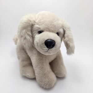 May include: A plush white dog toy with black eyes and a black nose. The dog is sitting with its legs tucked under its body.