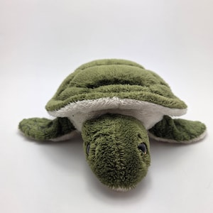 May include: A plush green turtle toy with a textured shell and white underside. The turtle has small black eyes and flipper-like appendages. The toy is designed to resemble a sea turtle.