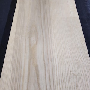 Puede incluir: Primer plano de una tabla de madera de color claro con un patrón de vetas natural. La madera tiene una superficie lisa y un tono claro y neutro, con sutiles variaciones de color y textura. La veta corre verticalmente.