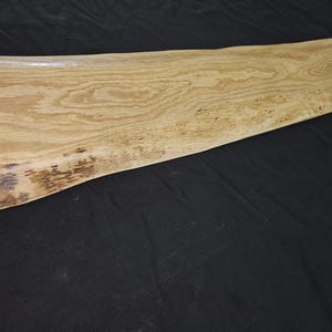 May include: A light-colored, rectangular wooden serving board with a natural edge. The wood grain is visible, and the board has a smooth, finished surface. The board is approximately 30 inches long.