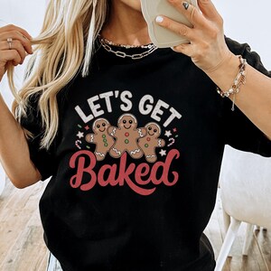 May include: Black t-shirt with a festive design featuring three gingerbread men and the text "Let's Get Baked".