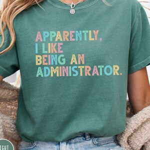 May include: Light green t-shirt with the text "Apparently, I Like Being an Administrator" in pastel colours. The shirt has a crew neck and short sleeves. The words "Light Green" are in a circle at the bottom left.