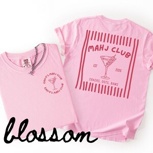 Puede incluir: Dos camisetas rosa claro con el texto "MAHJ CLUB" y un dise&ntilde;o de copa de c&oacute;ctel. Una camiseta tiene el texto "EMILY'S MAHJ CLUB" y un dise&ntilde;o de copa de c&oacute;ctel. La palabra "blossom" est&aacute; escrita en cursiva en la parte inferior.