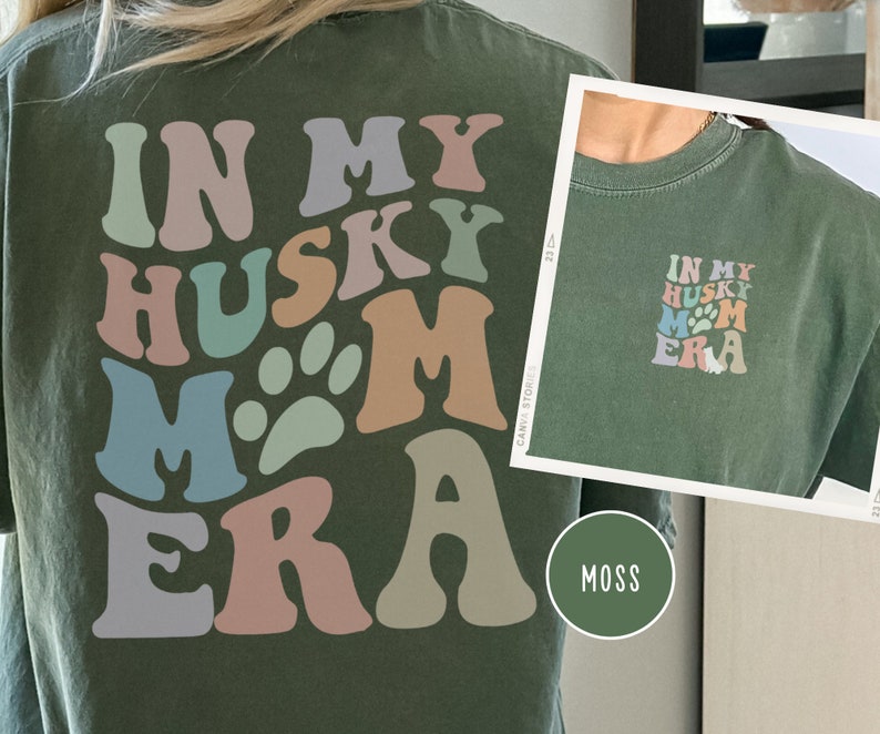 May include: A green t-shirt with the text "In My Husky Mom Era" in colorful, retro-style lettering. The text includes a paw print graphic.
