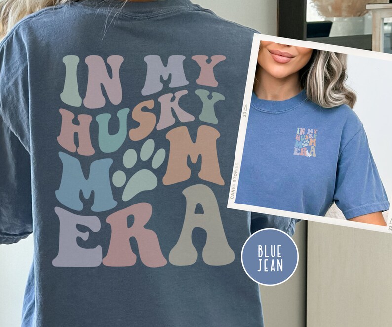 May include: A blue jean t-shirt with the text "In My Husky Mom Era" in colorful retro letters. The shirt is shown on a model wearing the shirt.
