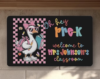 May include: Black rectangular sign with a cartoon goose wearing sunglasses, a pink bow, and a backpack. The sign reads "Oh hey Pre-K welcome to Mrs. Johnson's classroom" in colorful text, with a pink and white checkered border.
