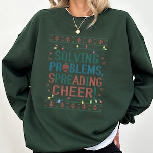 May include: Green Christmas sweater with the text "Solving Problems, Spreading Cheer!" in a festive font with colorful lights and ornaments.