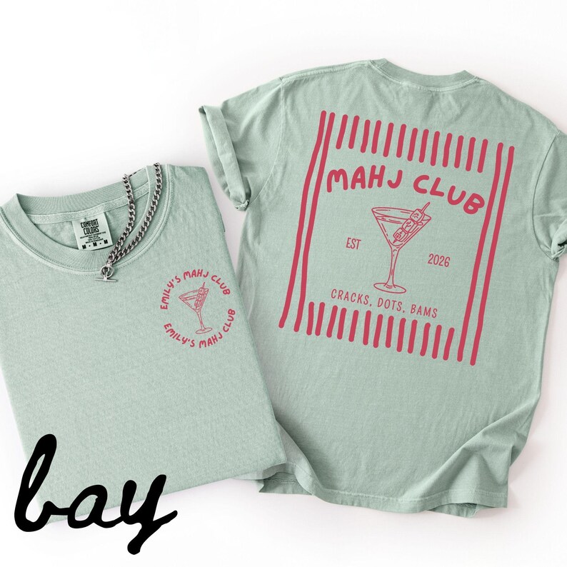 Puede incluir: Dos camisetas verde claro con gr&aacute;ficos rojos. Una camiseta tiene un peque&ntilde;o dise&ntilde;o circular con texto y una copa de c&oacute;ctel. La otra camiseta tiene un dise&ntilde;o m&aacute;s grande en la espalda con las palabras "MAHJ CLUB" y una copa de c&oacute;ctel.