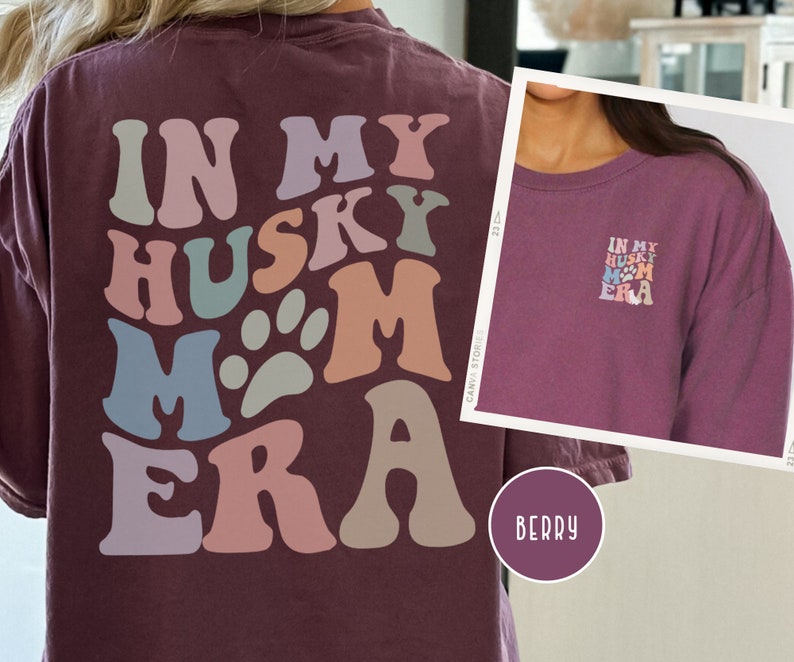 May include: A maroon long-sleeve t-shirt with the text "In My Husky Mom Era" in a retro, colorful font. The text is arranged in a circular pattern with paw prints.