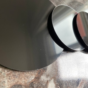 Puede incluir: Tres discos circulares negros de diferentes tamaños, dispuestos en semicírculo sobre una superficie marrón moteada.