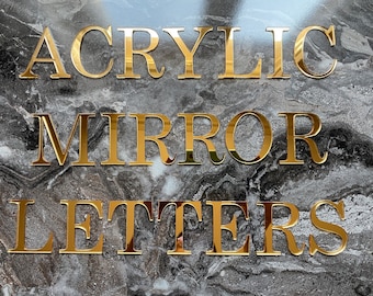 May include: Gold acrylic mirror letters spelling out "Acrylic Mirror Letters" on a black and white marble background.