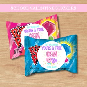 May include: Two Ring Pop candies in pink and blue wrappers with Valentine's Day stickers. The stickers say "Hey Valentine! You're a True Gem" with gem illustrations. Each candy is 0.5 oz (14g).