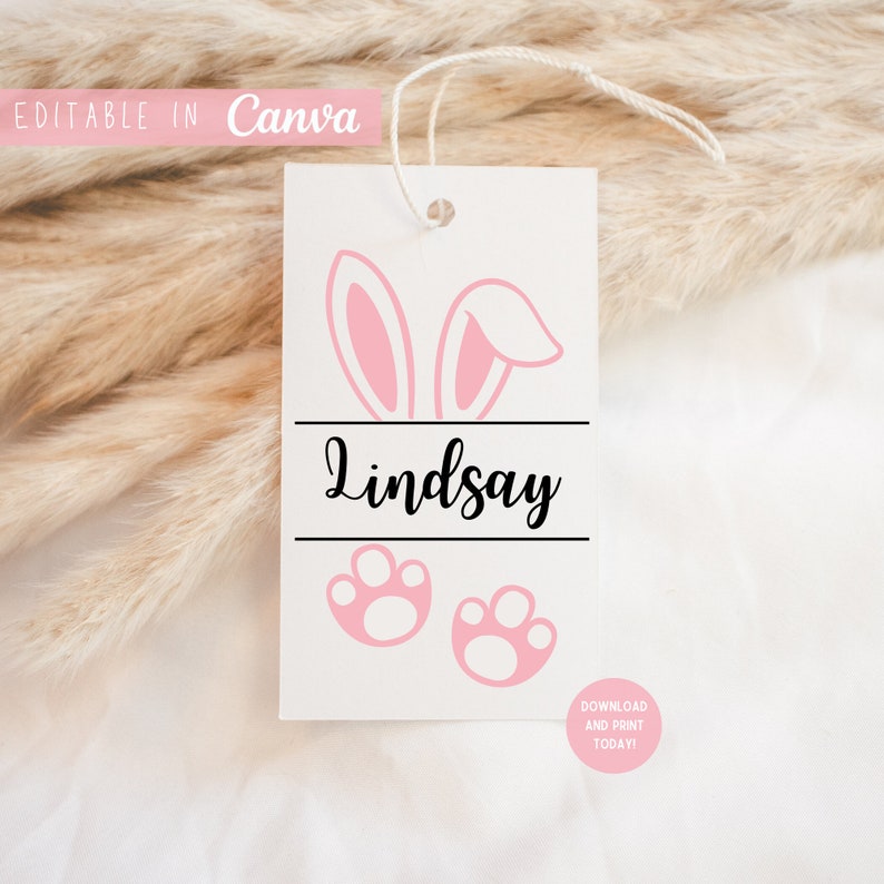 May include: A white printable tag with pink bunny ears, paw prints, and the name "Lindsay" in black cursive text. The tag has a hole at the top for string or ribbon.