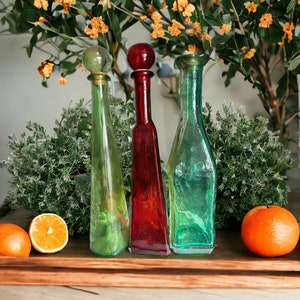 May include: Three glass bottles with different colored liquids, a green bottle, a red bottle, and a blue bottle. The bottles are on a wooden tray with two oranges on the tray.