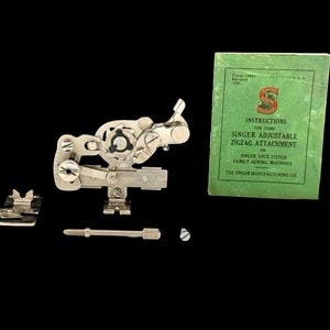 May include: A silver metal Singer adjustable zigzag attachment for sewing machines, accompanied by two small metal presser feet, a long thin metal screw, a small screw, and a green instruction booklet titled Instructions for Using Singer Adjustable Zigzag Attachment for Singer Lock Stitch Family Sewing Machines.