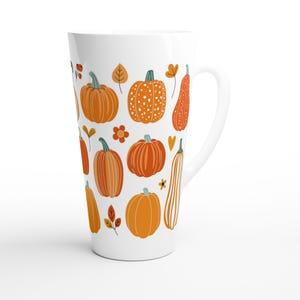 May include: White ceramic latte mug decorated with orange pumpkins, leaves, and flowers. The mug features various pumpkin designs, including dotted and striped patterns, perfect for autumn or fall-themed decor.