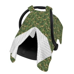 May include: A baby car seat cover with a jungle-themed design. The cover has a green background with a repeating pattern of leaves and cheetahs. The interior lining is white and textured.