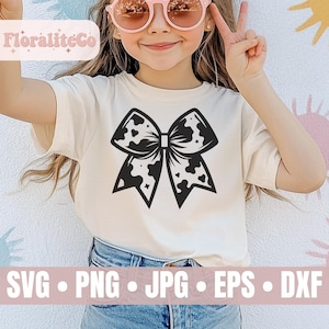 Op de afbeelding: Een wit T-shirt met een zwart-witte koe-print strikdesign. Het ontwerp is gecentreerd op het shirt. Het shirt wordt gedragen door een kind.