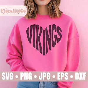 May include: A bright pink long-sleeve sweatshirt featuring a dark purple graphic of the word VIKINGS shaped into a heart. The text is centred on the chest. The sweatshirt has a crew neckline and long sleeves, providing a casual and comfortable fit.