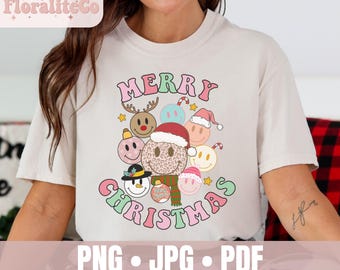 Puede incluir: Una camiseta beige de manga corta con un estampado gráfico que incluye el texto MERRY CHRISTMAS en rosa y verde. El diseño presenta varias caras sonrientes con motivos navideños, como astas de reno, un gorro de Papá Noel y un muñeco de nieve.