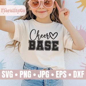 May include: A white t-shirt with the text "Cheer Base" in black with a heart symbol. The shirt is being worn by a child with blonde hair and sunglasses.