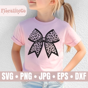 Op de afbeelding: Een roze T-shirt met een zwart-wit luipaardprint strikdesign. Het ontwerp is gecentreerd op het shirt. Het shirt wordt gedragen door een kind.