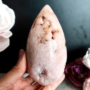 Puede incluir: Un cristal rosa en forma de l&aacute;grima con una superficie rugosa y texturizada. El cristal tiene un color rosa claro con un toque de marr&oacute;n.