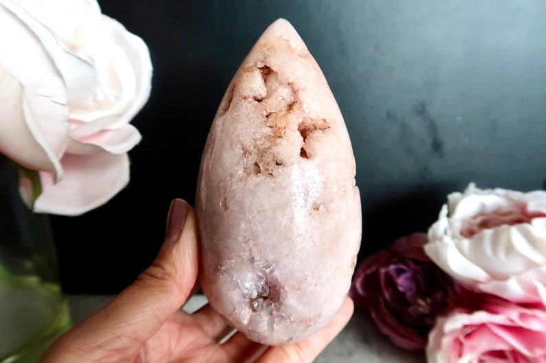 Puede incluir: Un cristal rosa en forma de l&aacute;grima con una superficie rugosa y texturizada. El cristal tiene un color rosa claro con un toque de marr&oacute;n.