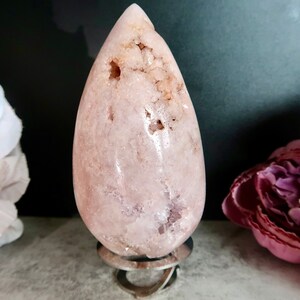 Puede incluir: Un cristal rosa en forma de l&aacute;grima sobre un soporte de metal. El cristal tiene una superficie rugosa y texturizada y es transl&uacute;cido.