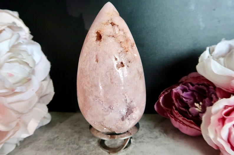 Puede incluir: Un cristal rosa en forma de l&aacute;grima sobre un soporte de metal. El cristal tiene una superficie rugosa y texturizada y es transl&uacute;cido.