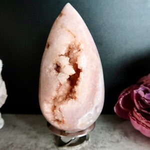 Puede incluir: Una geoda rosa en forma de l&aacute;grima con un interior forrado de cristales. La geoda est&aacute; sobre un soporte plateado.