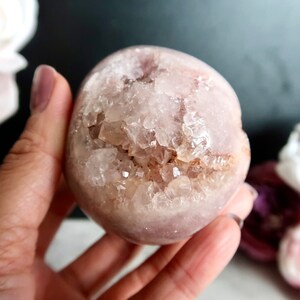Puede incluir: Una esfera de cristal rosa y blanca con un interior de geoda. La esfera es lisa y pulida, con una textura natural y rugosa en el interior. La geoda est&aacute; llena de peque&ntilde;os cristales transparentes.