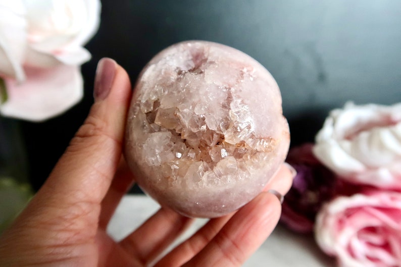 Puede incluir: Una esfera de cristal rosa y blanca con un interior de geoda. La esfera es lisa y pulida, con una textura natural y rugosa en el interior. La geoda est&aacute; llena de peque&ntilde;os cristales transparentes.