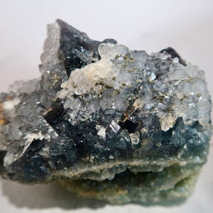 May include: A close-up of a raw, uncut fluorite crystal cluster. The crystal features a mix of dark blue, clear, and light green hues, with small, sparkling inclusions. The rough texture and natural formation are clearly visible.